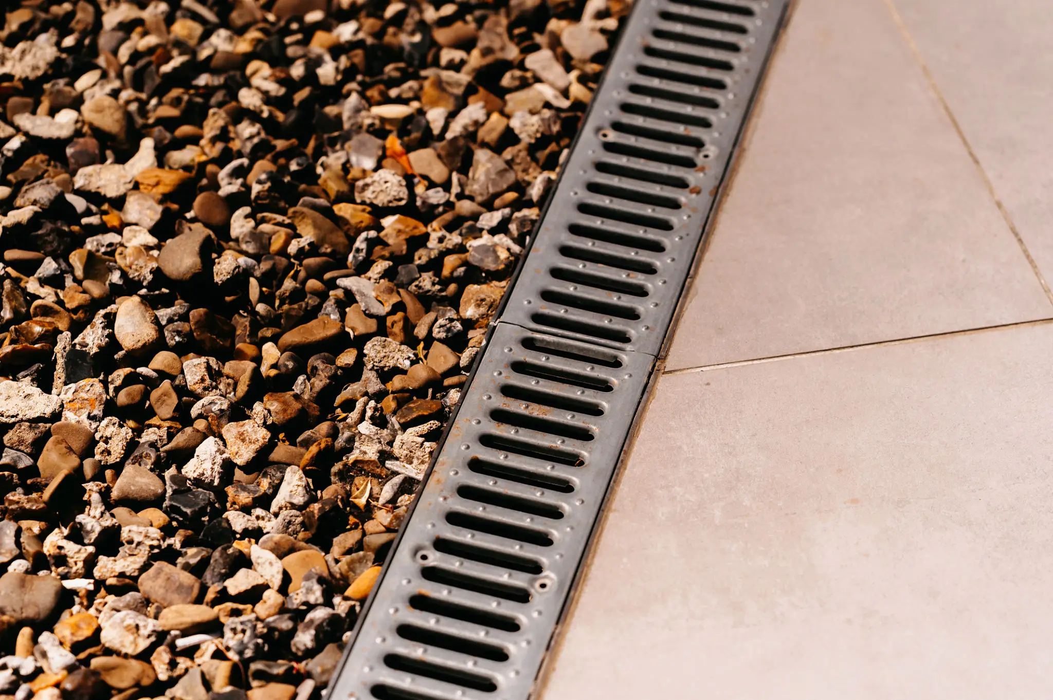 Metal drainage grate separating gravel and pavement.