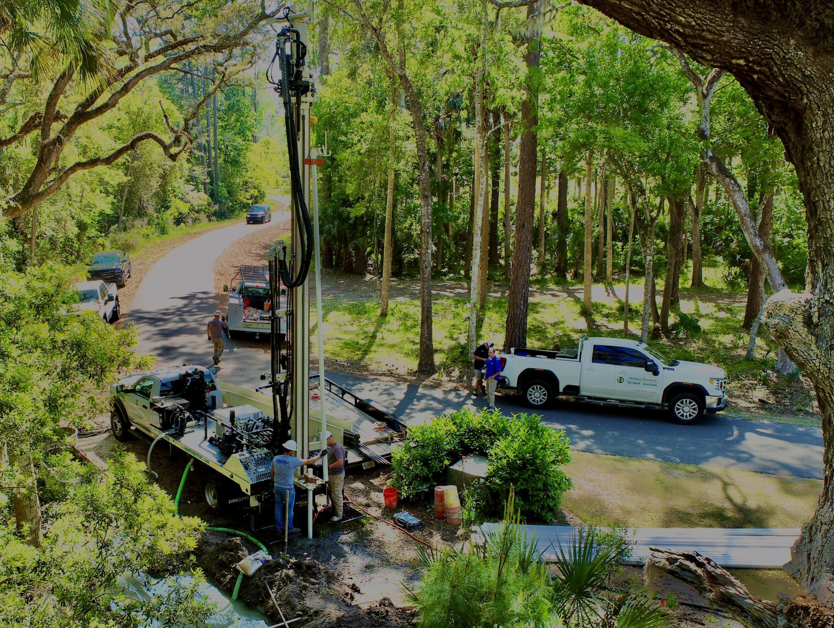 A white truck parked on a driveway near a garden with trees.