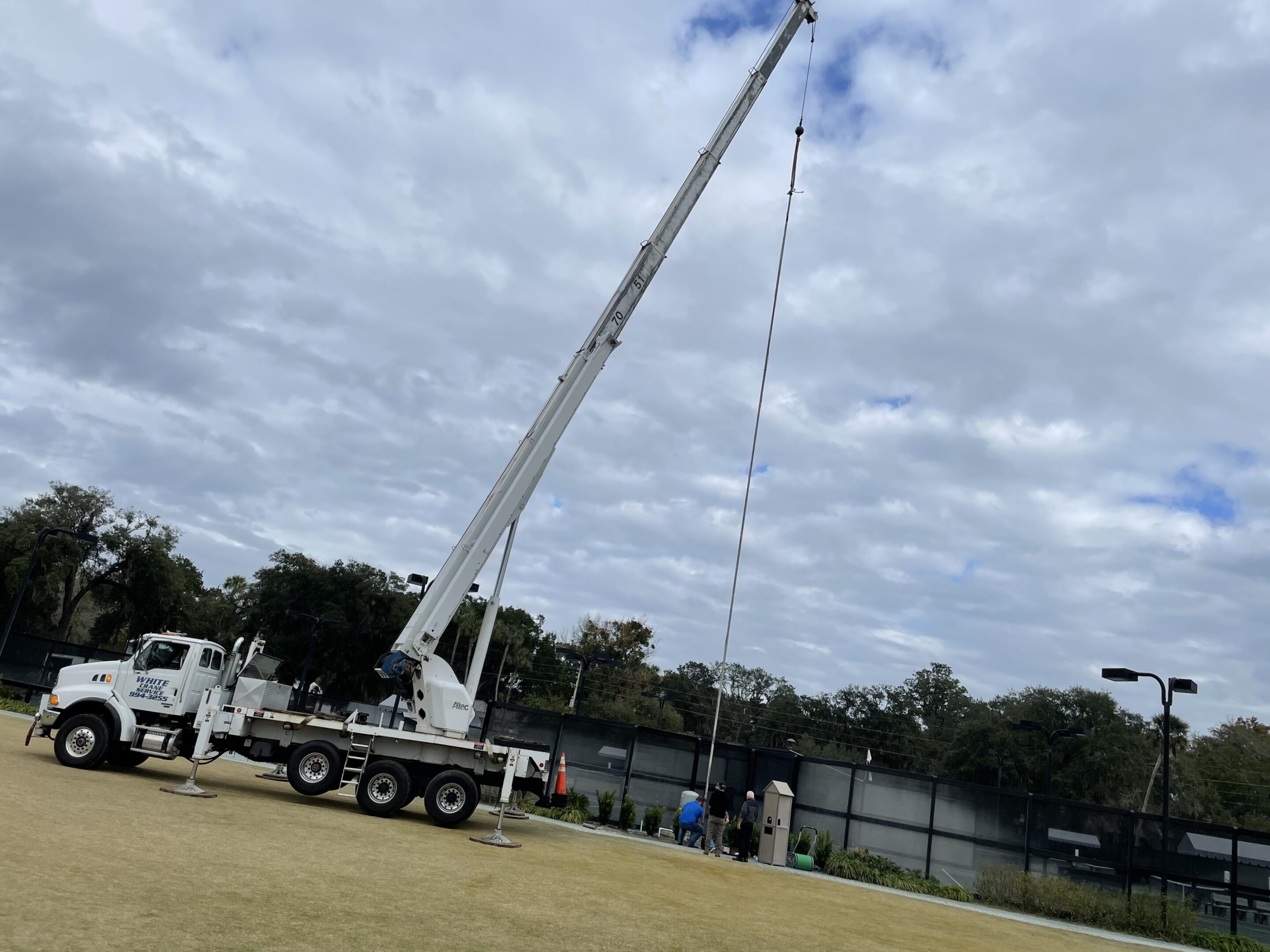 A mobile crane lifting equipment on a field under a cloudy sky.